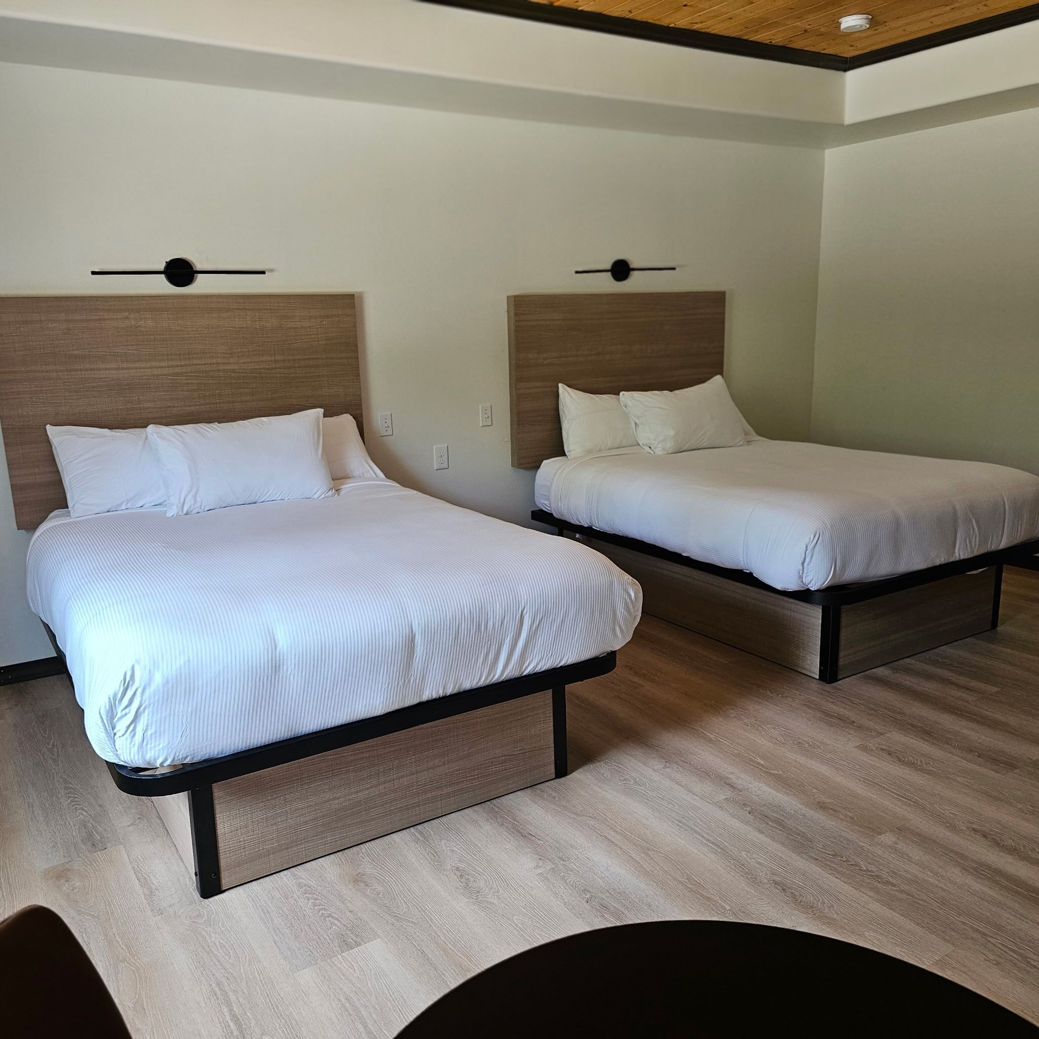Dos camas con cabeceros de madera, suelo de madera y techo con una lámpara empotrada.