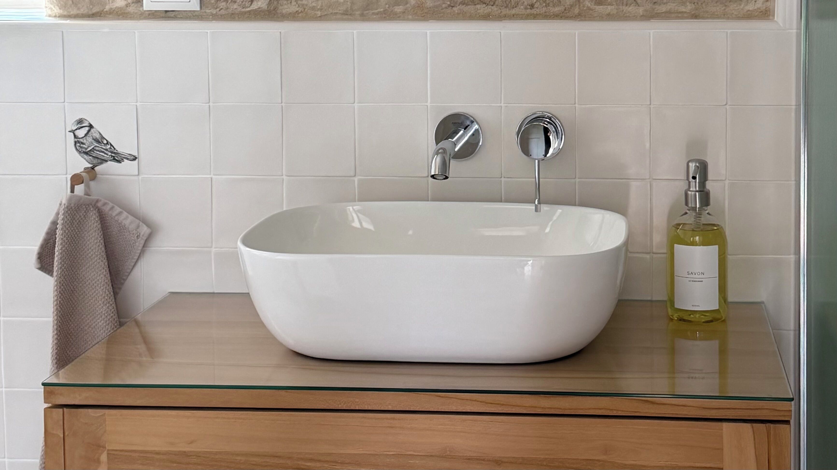A bathroom with a white sink, a mirror, and a bottle of Savon soap on a glass countertop.