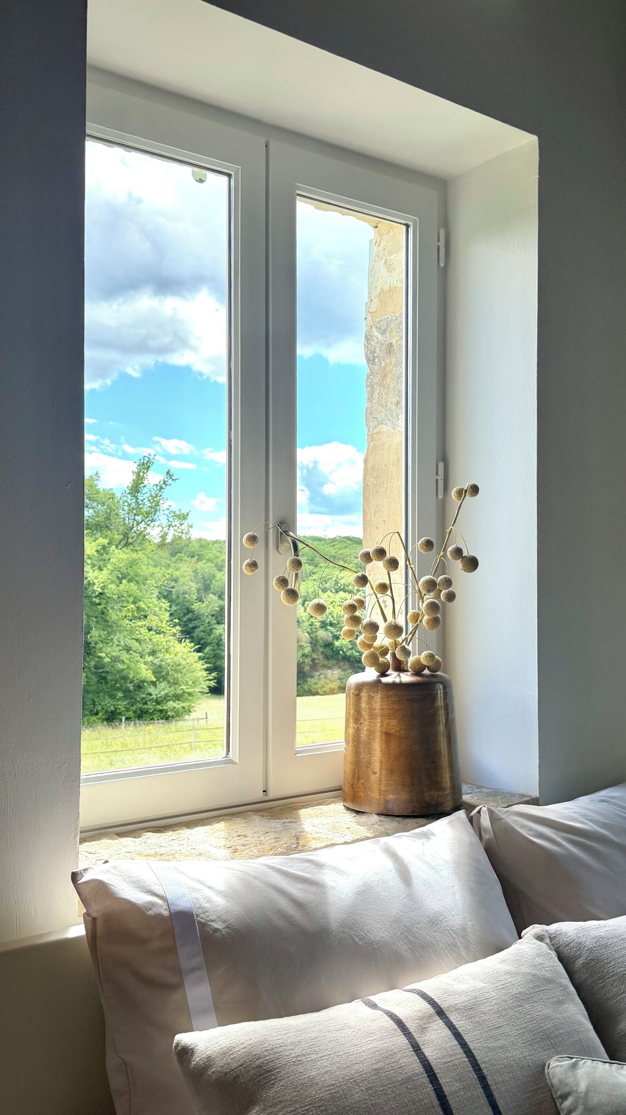 Una habitación con un ventanal grande, un taburete de madera y vistas al verdor.