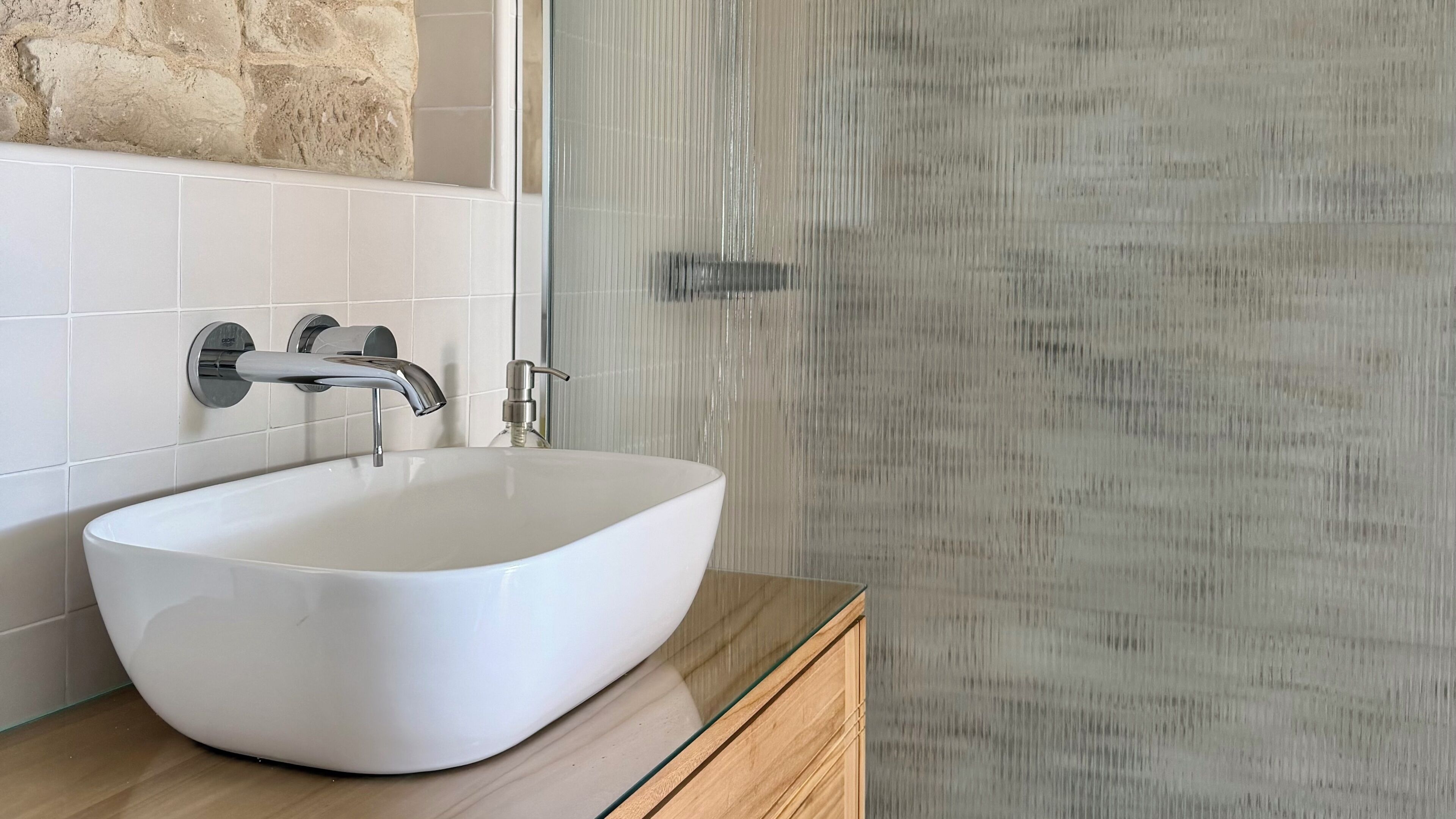 Un baño con lavamanos blanco, ducha con puerta de vidrio y pared de acento de piedra.