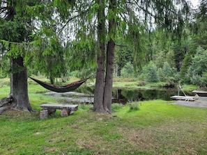 Una hamaca entre árboles, un banco de madera y un muelle junto a un lago tranquilo.