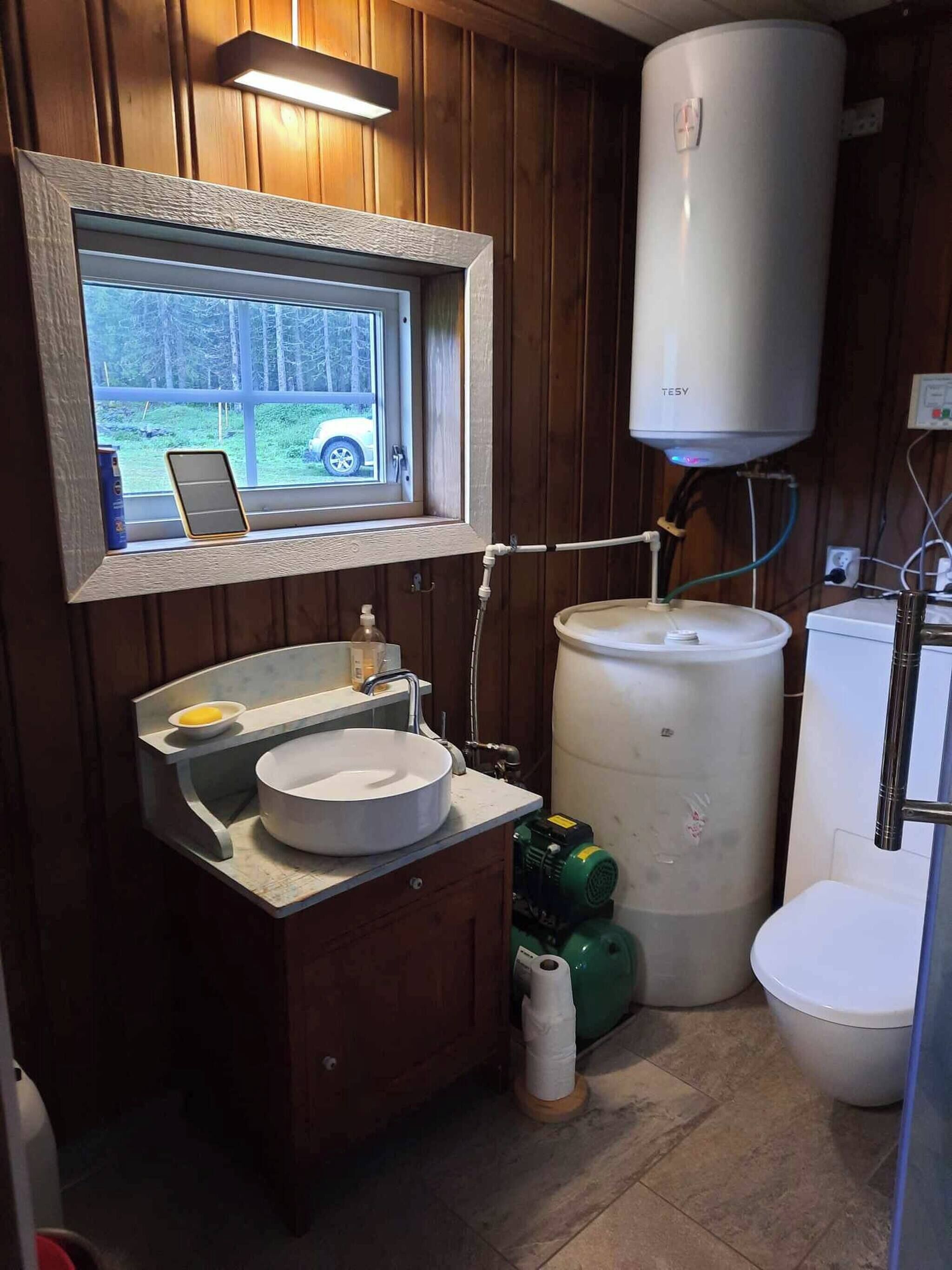 Un baño con ventana, lavamanos, inodoro y calentador de agua.
