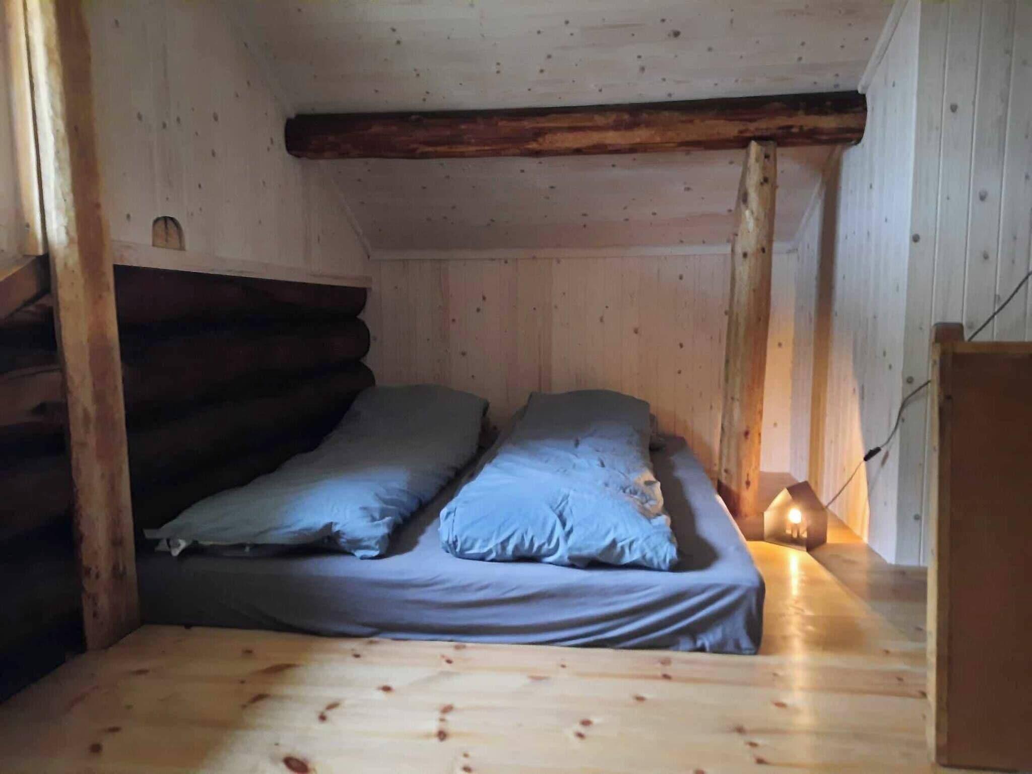 Ein kleiner, gemütlicher Raum mit einem Holzbett und einem Nachttisch mit Lampe.