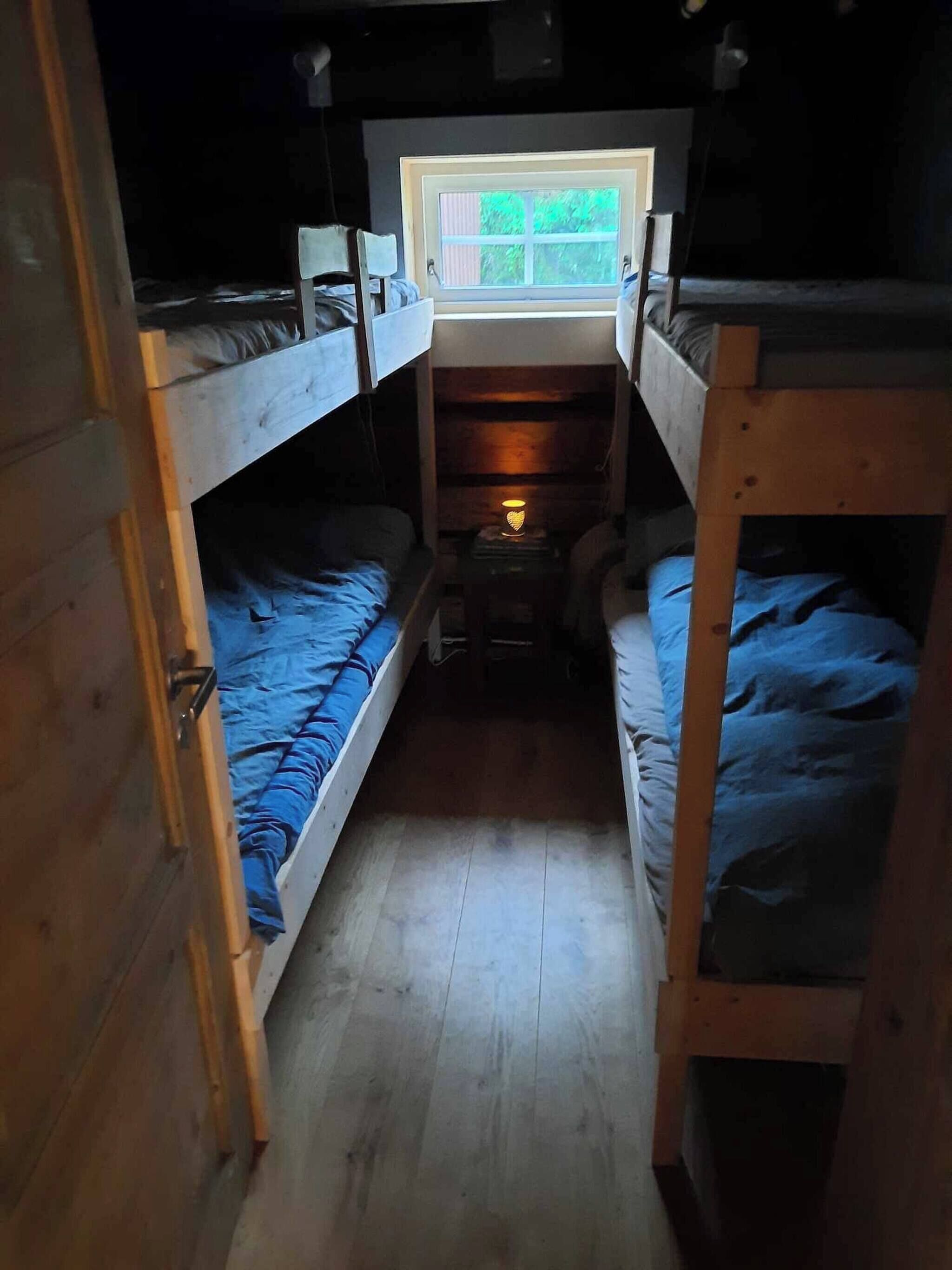 Una habitación pequeña con literas, un ventanal y una mesita de noche con lámpara.