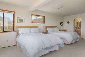 A bedroom with two beds, a window, a bedside table with a lamp, and a mirror on the wall. - Ocean House, by Vinifera Homes (Gualala)