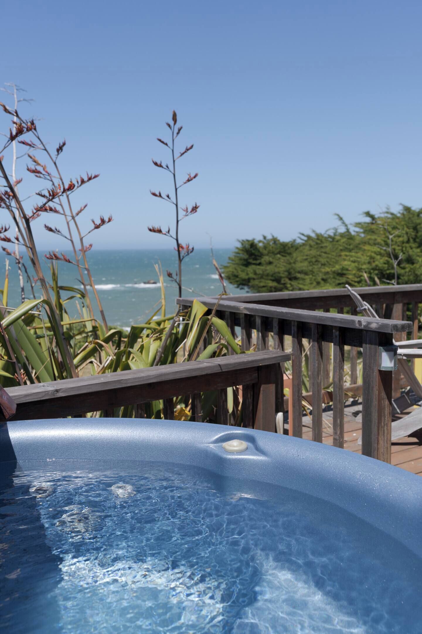 A hot tub with a clear view of the ocean and a wooden deck.