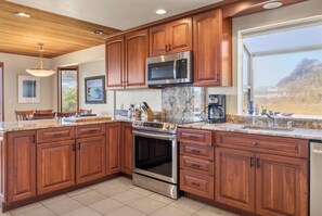 A modern kitchen with wooden cabinets, stainless steel appliances, and a large window offering a view. - Ocean House, by Vinifera Homes (Gualala)