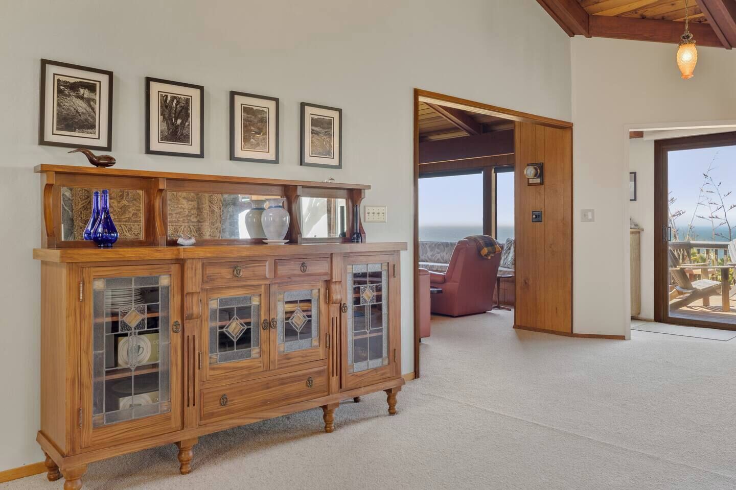 Un meuble en bois avec des portes en verre, un fauteuil rouge et des tableaux encadrés accrochés au mur.