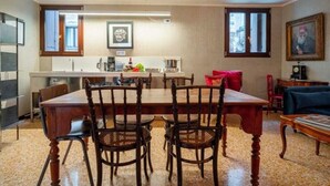 A dining area with a wooden table and chairs, a kitchen in the background, and a chandelier. - Grand Canal Palazzo Retreat with Private Canal Views in San Marco (Venezia)