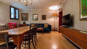 A room with a wooden dining table, chairs, a sofa, a TV, and a lamp. - Grand Canal Palazzo Retreat with Private Canal Views in San Marco (Venezia)