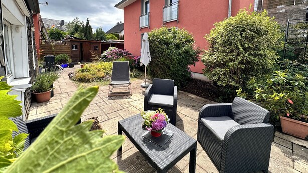 A patio with outdoor furniture, a small table with flowers, and a red building in the background.