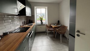 A compact kitchen with a window, a dining area with chairs, and a refrigerator.