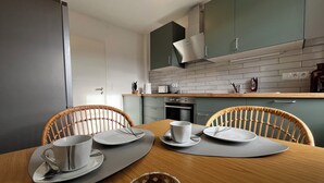 A modern kitchen with a wooden dining table, two wicker chairs, and a coffee maker.