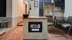 Een hotel receptie met een marmeren balie, ingelijste foto's, een brandblusser en een zwarte kast.