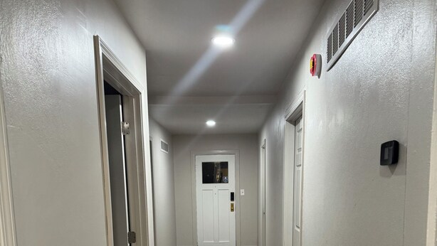 Un couloir doté d’un plancher en bois, de murs blancs et de portes donnant accès aux pièces.
