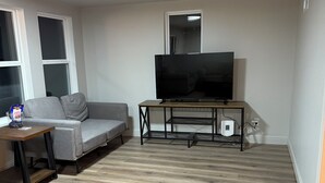 Un salon avec un canapé, une table basse, un téléviseur posé sur un meuble et un plancher en bois.