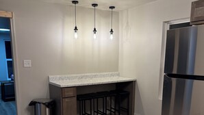 Une cuisine moderne avec un réfrigérateur en acier inoxydable, un plancher en bois et des luminaires suspendus.