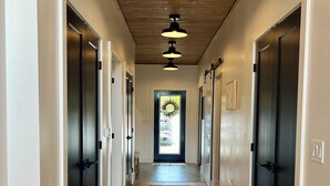 A hallway with wooden floors, black doors, and pendant lighting.
