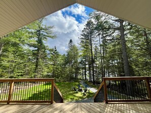 A deck with a view of a forested area, including tall trees and a grassy lawn.