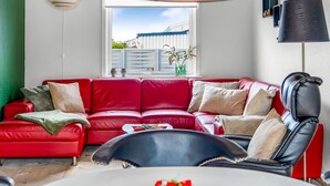 A red leather sofa, a black leather chair, a white table with a vase of flowers, and a window with a view of a building and plants. - "Lotte" - 1.5km from the sea by Interhome (Skagen)