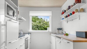 A compact kitchen with white cabinetry, a window with a view of greenery, a wooden countertop, and a built-in coffee maker. - "Lotte" - 1.5km from the sea by Interhome (Skagen)