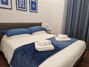 Habitació d'hotel amb llit doble, dues almoades, una petita taula de nit, una làmpada i dues tovelloles.
