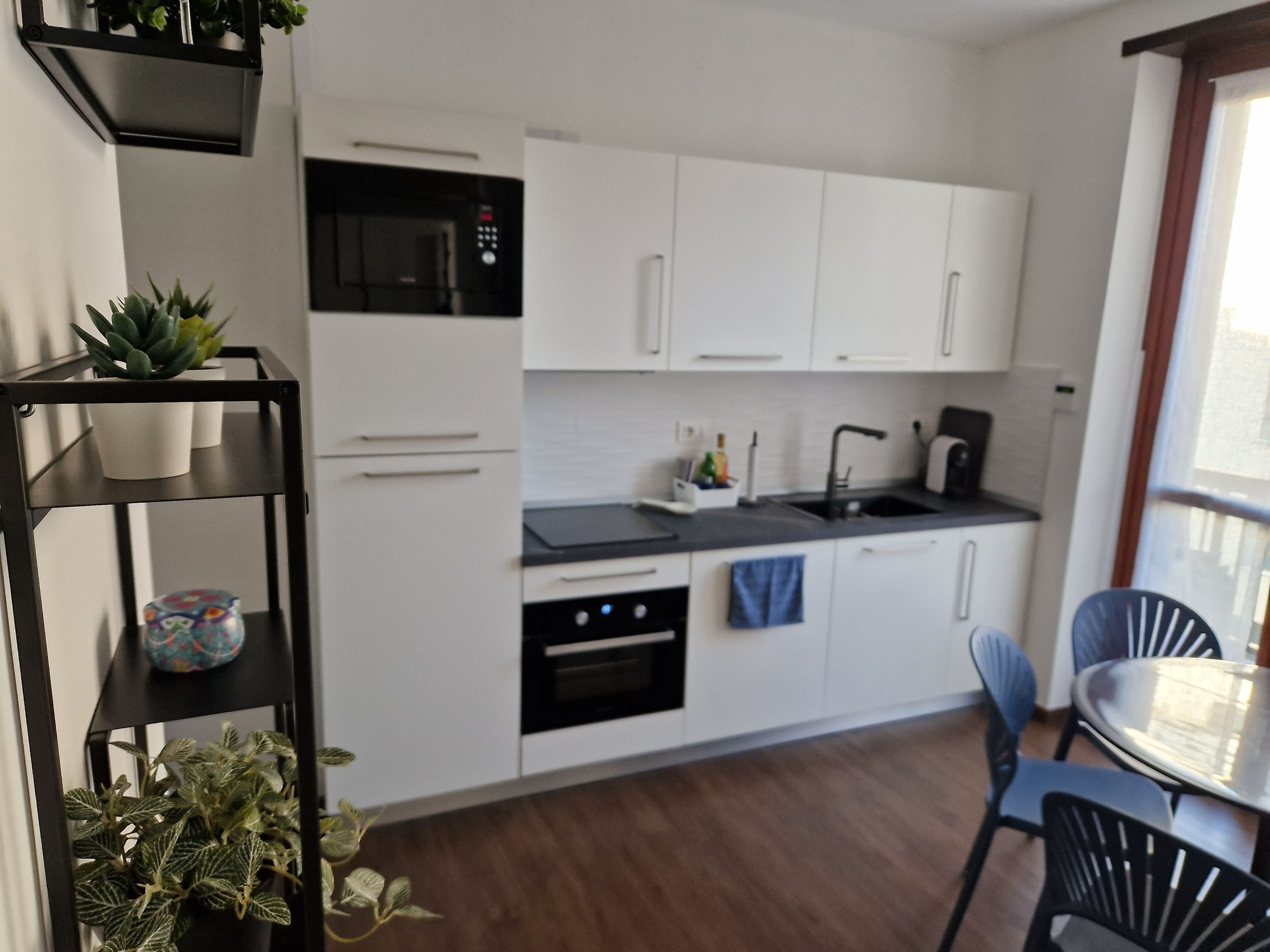 Moderni keittiö, jossa on valkoiset kaapit, musta työtaso sekä ruokailutila, jossa on pöytä ja tuolit.