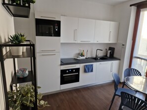 Moderni keittiö, jossa on valkoiset kaapit, musta työtaso sekä ruokailutila, jossa on pöytä ja tuolit.