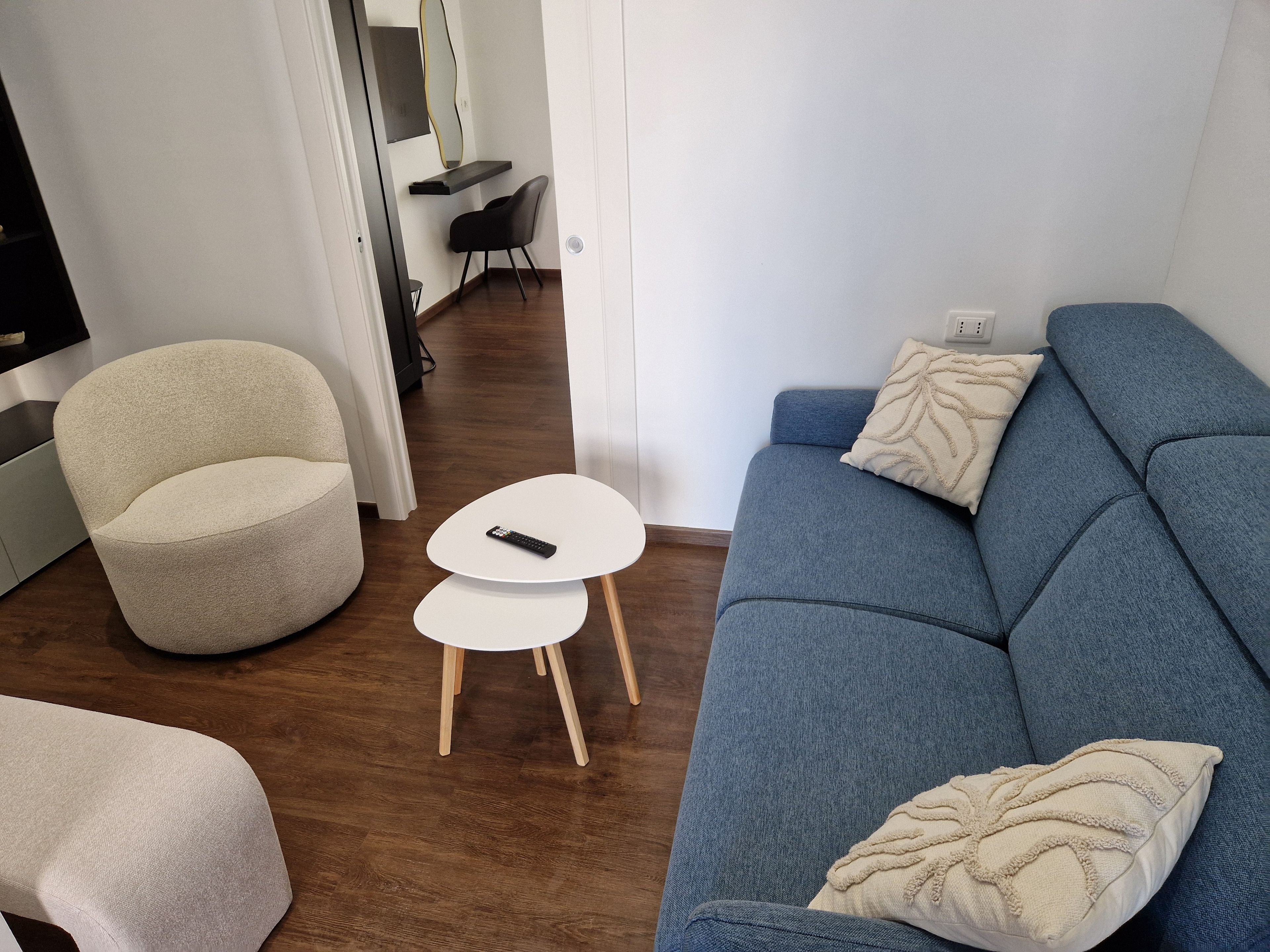Un soggiorno moderno con un divano blu, una poltrona beige e un tavolino bianco con un telecomando.
