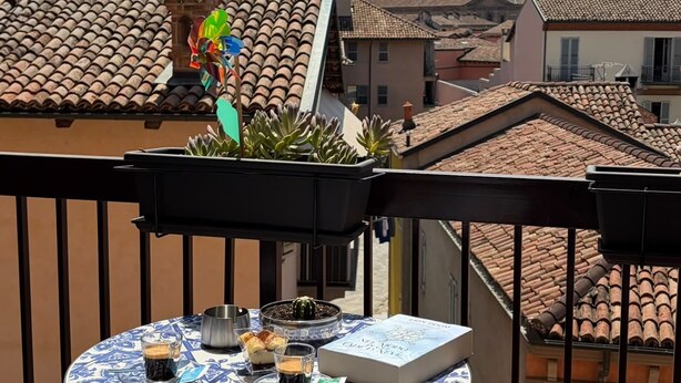 En balkon med et bord dækket til to, en potteplante og udsigt til bygninger med terracotta tag.