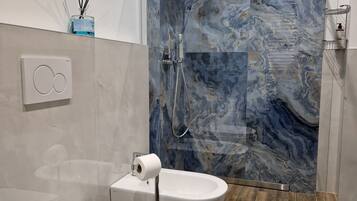 Un bagno moderno con parete doccia in marmo, un water e un bidet.