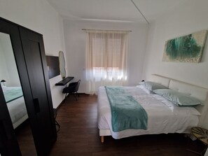 A hotel room with a bed, a desk, a chair, a wardrobe, and a window with curtains.