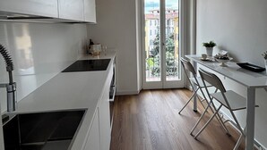 Eine moderne Küche mit weißen Schränken, ein Essbereich mit Tisch und Stühlen sowie ein Ausblick durch eine Glastür ins Freie.