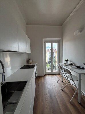 Eine moderne Küche mit weißen Schränken, ein Essbereich mit Tisch und Stühlen sowie ein Ausblick durch eine Glastür ins Freie.