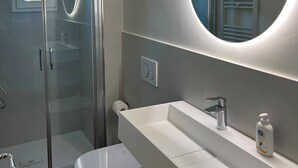 Ein modernes Badezimmer mit einer einteiligen Duschkabine, Toilette, Waschbecken und einem Spiegel darüber sowie einem Handtuchhalter.