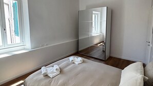Ein Schlafzimmer mit einem Bett, einem großen Spiegel, einem Fenster und einer Tür.