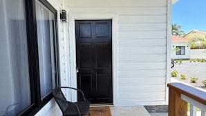 A balcony with a black door, a chair, and large green plants. - Leleka's Cabin - E4 (Flowers Bay)
