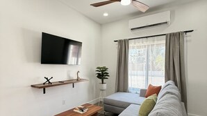 A modern living room with a grey sofa, a wooden coffee table, a mounted TV, and a ceiling fan. - Leleka's Cabin - E4 (Flowers Bay)