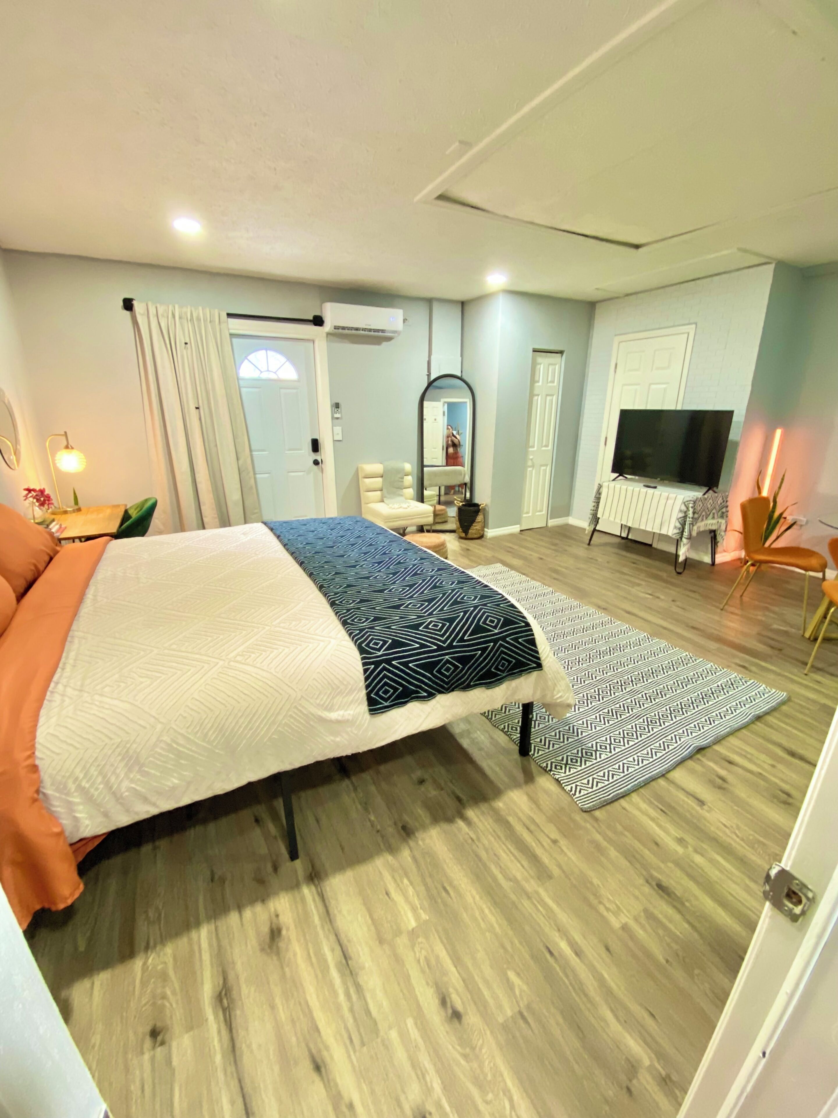 Un dormitorio con cama, televisión, espejo y puerta.