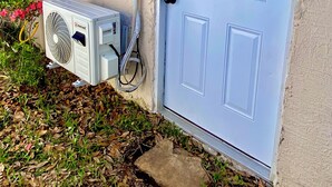 Ein Haus mit einer weißen Tür, einer Klimaanlage und elektrischen Schaltkästen an der Außenwand.