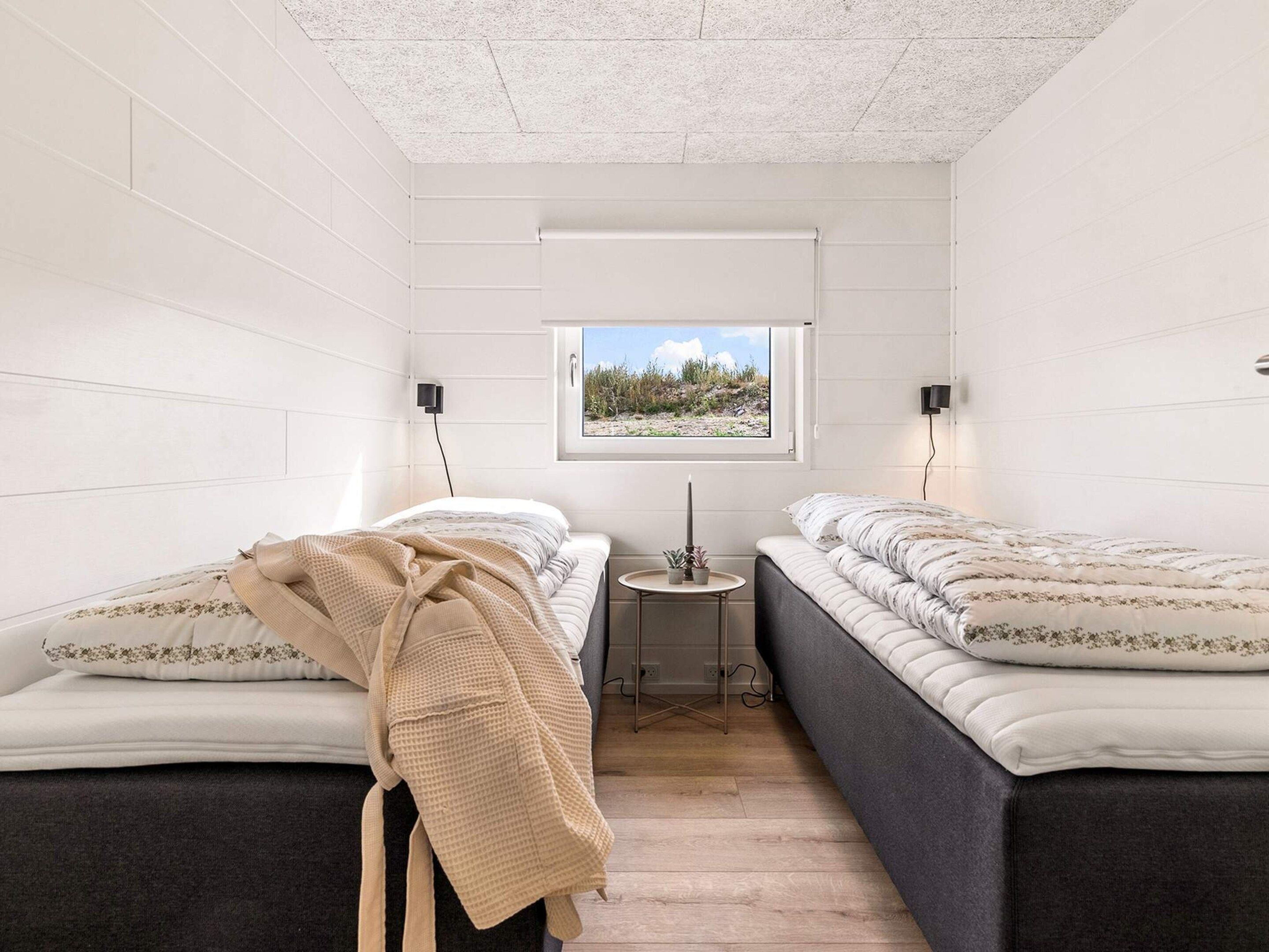 A bedroom with two beds, a small table, a window with a view, and a ceiling with a textured pattern.