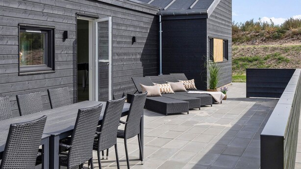 An outdoor patio area with a dining table and chairs, a sofa, and a small garden. - 5 Star Holiday Home in Glesborg (Glesborg)