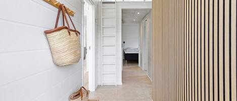 Un pasillo con un banco de madera, un bolso tejido colgante y una pared de listones de madera.
