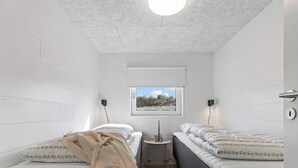 A small, modern bedroom with two beds, a window with a view, and a small table with a lamp. - 5 Star Holiday Home in Glesborg (Glesborg)