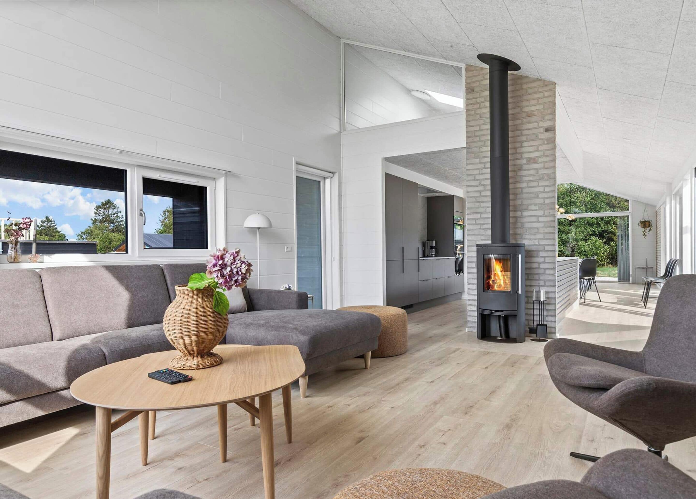 Un salon moderne avec une cheminée, des canapés gris, une table basse et une vue sur l’extérieur.
