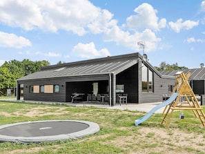 A modern building with a covered outdoor seating area, a trampoline, and a wooden slide. - 5 Star Holiday Home in Glesborg (Glesborg)