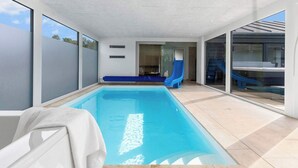 An indoor swimming pool with a blue slide, a bench, and a view of the outside. - 5 Star Holiday Home in Glesborg (Glesborg)