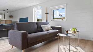 A modern living room with a grey sofa, a small round table, and a view of the outdoors through a window. - 5 Star Holiday Home in Glesborg (Glesborg)