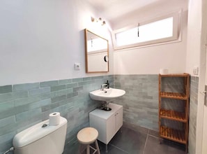 Ein Badezimmer mit Toilette, Waschbecken und Ablagefläche aus Holz, mit einer gefliesten Spritzwand und einem Fenster.