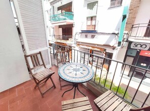 Ein Balkon mit rundem Tisch und zwei Stühlen, einem Kachelboden und Blick auf ein Gebäude mit Balkonen und einem Schild mit der Aufschrift '500 GAMING'.